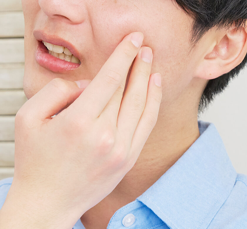 歯の痛みで頬をおさえる男性のイメージ